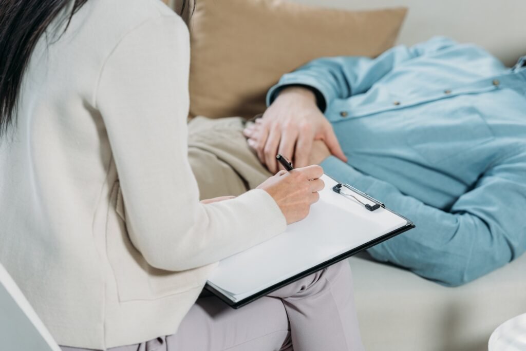 cropped shot of psychotherapist writing on clipboard and male patient lying on couch